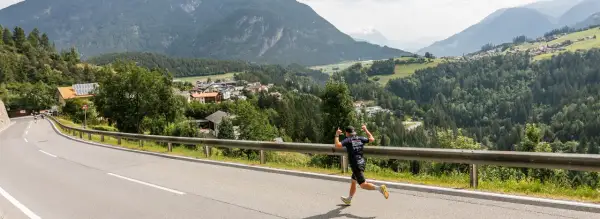 Läufer beim Pitztal Marathon mit Daumen hoch, im Hintergrund ein malerisches Bergdorf.